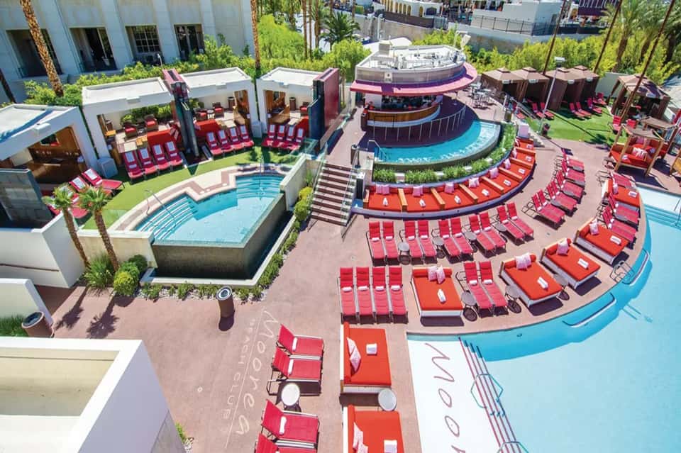 Aerial resort pool complex with red loungers, curved pools, and palm trees