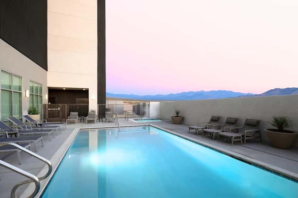 Modern hotel pool at dusk with mountain views, lounge chairs, and illuminated water