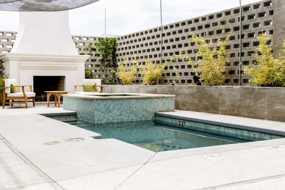 Residential rooftop with sunken pool, modern fireplace, concrete walls, and landscape background