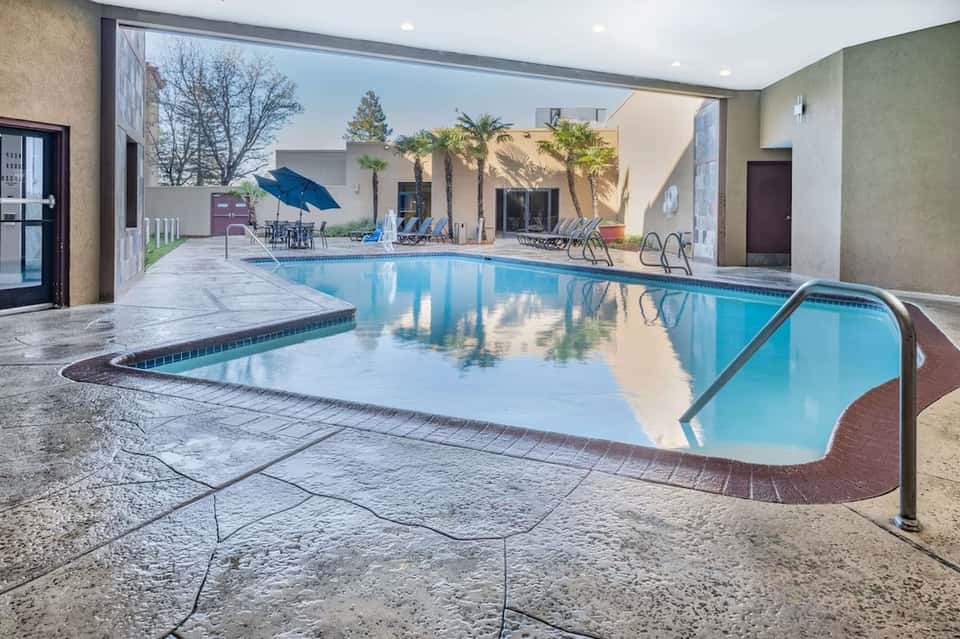 Indoor pool with glass enclosure, lounge chairs, and surrounding building architecture