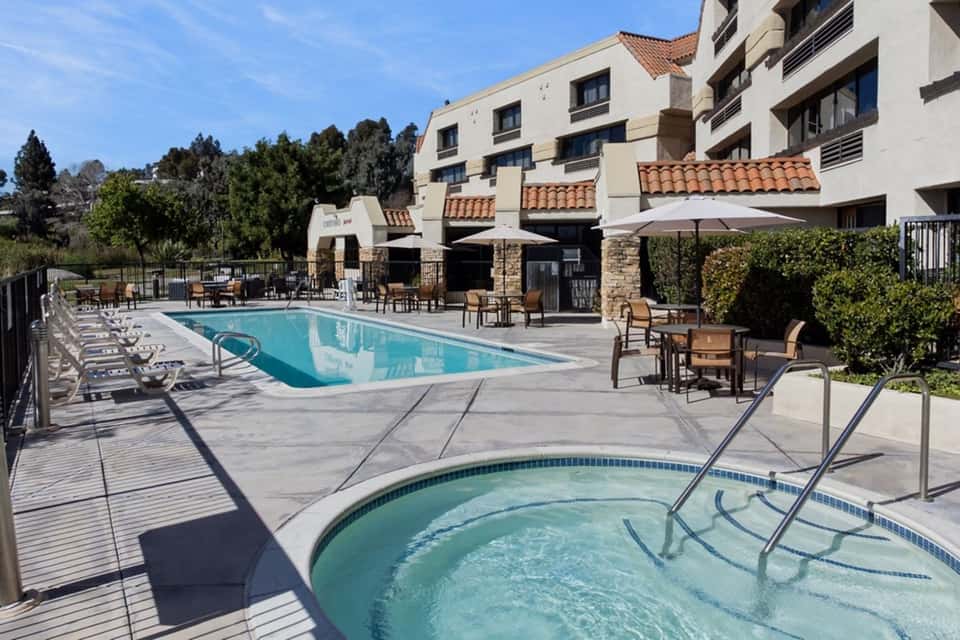 Resort pool area with spa, lounge chairs, umbrellas, and Spanish-style building architecture