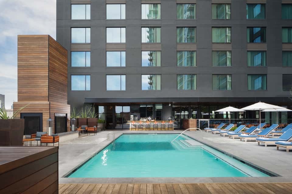 Modern hotel exterior with dark facade, ground-level pool, lounge seating, and contemporary design