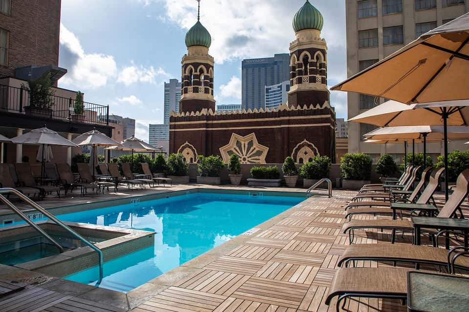 Hotel rooftop pool with tan umbrellas, lounge chairs, and ornate mosque backdrop in downtown setting