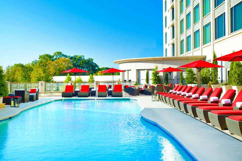 Luxury resort pool with red umbrellas and lounge chairs, modern building with green-trimmed windows