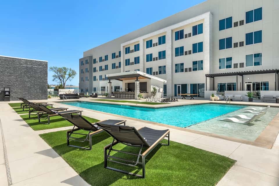 Resort outdoor pool with turquoise water, lounge chairs, modern white building, and clear sky