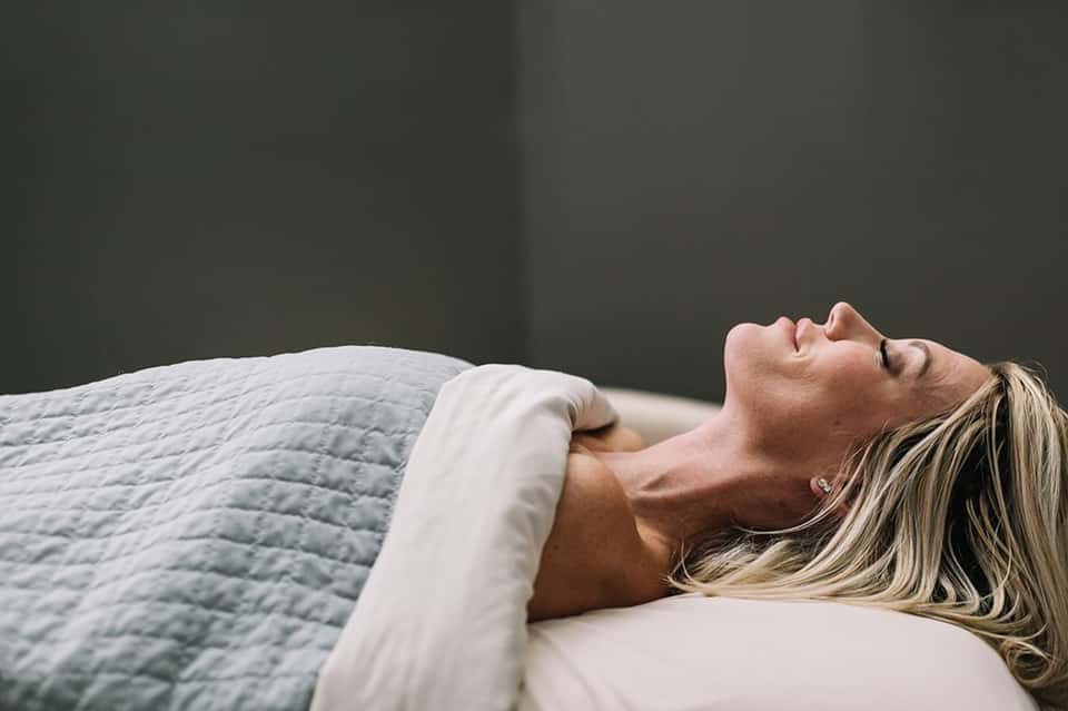 Woman relaxing in bed with soft white pillows and light green quilted bedding