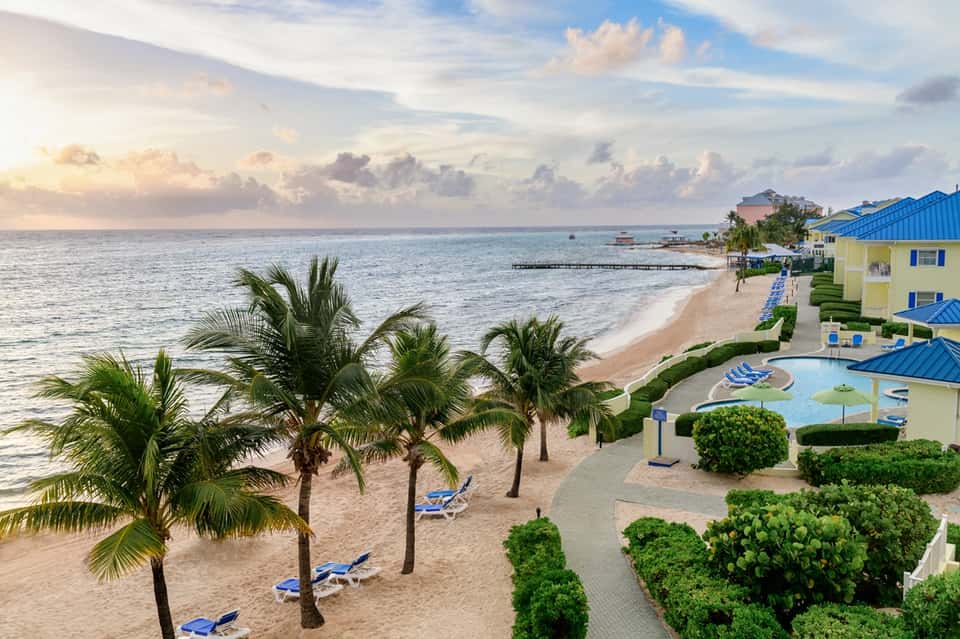 Beachfront resort with palm trees, white sand beach, pool area, and docks