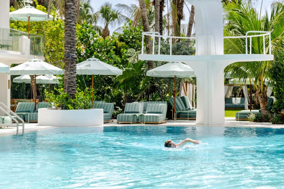 Contemporary pool with striped lounge chairs, umbrellas, white column, and palm trees
