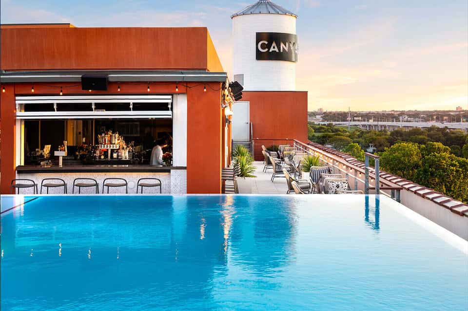 Rooftop pool with red bar building, water views, loungers, and sunset backdrop