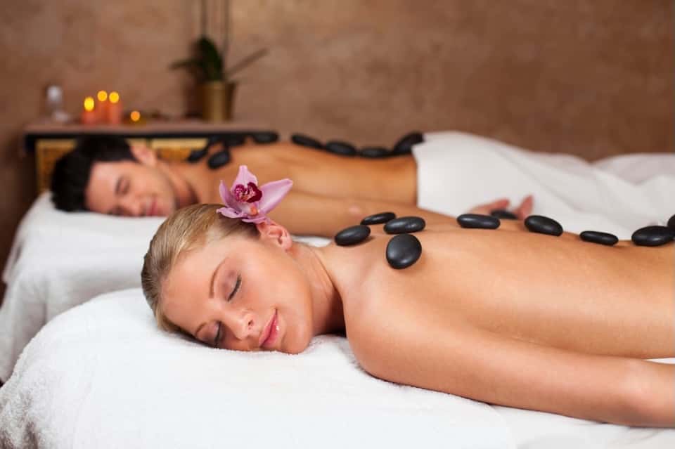 Spa massage treatment with heated stone therapy on client's back and orchid flower decoration