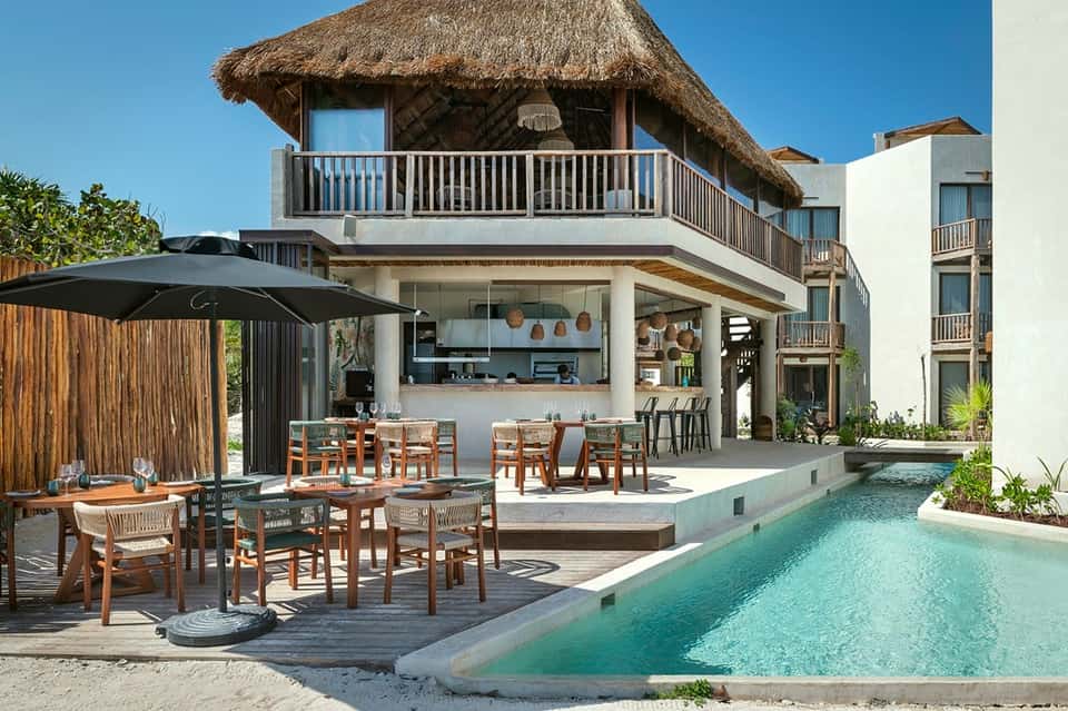 Luxury beachfront villa with thatched roof, infinity pool, and modern open-air dining area