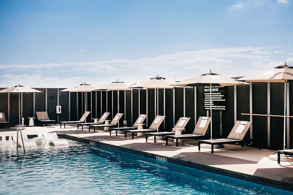 Modern rooftop pool deck with lounge chairs, umbrellas, dark privacy screens, and city skyline