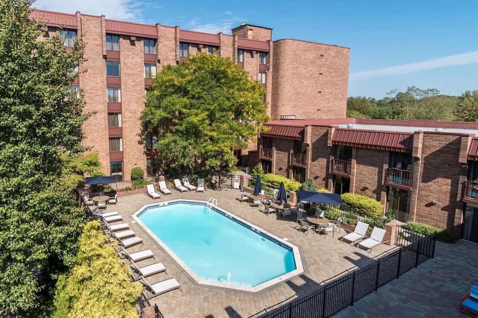 Courtyard pool at brick hotel surrounded by lounge chairs, building wings, and mature trees