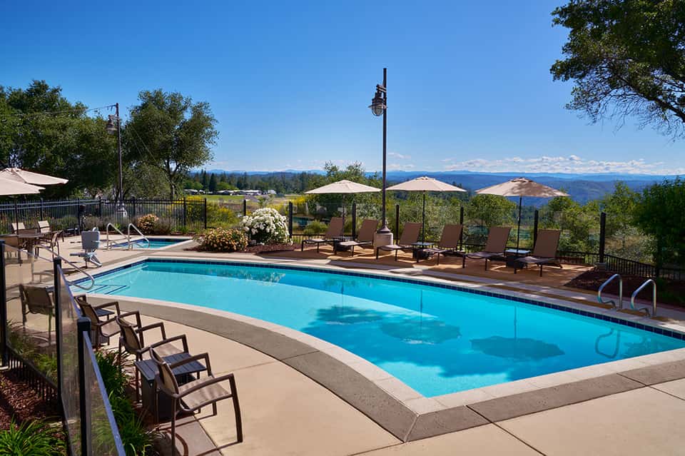 Mountain resort pool with blue water, lounge chairs, umbrellas, and scenic landscape vista