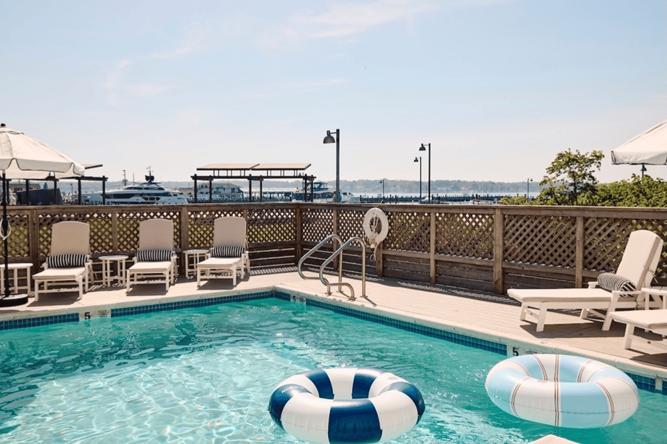 Rooftop pool deck with lounge chairs, striped umbrellas, lattice railing, and waterfront view