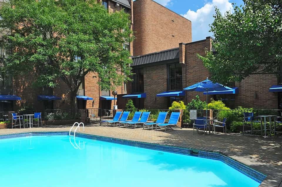 Urban courtyard pool surrounded by brick buildings with blue umbrellas and lounge seating