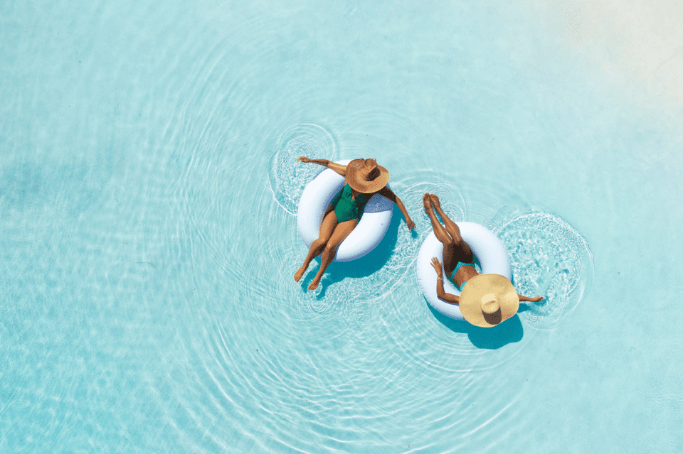 Aerial view of two people floating on white pool floats in crystal-clear turquoise water