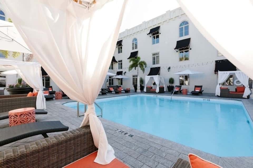 Courtyard pool with white draped cabanas, coral lounge chairs, and white building facade