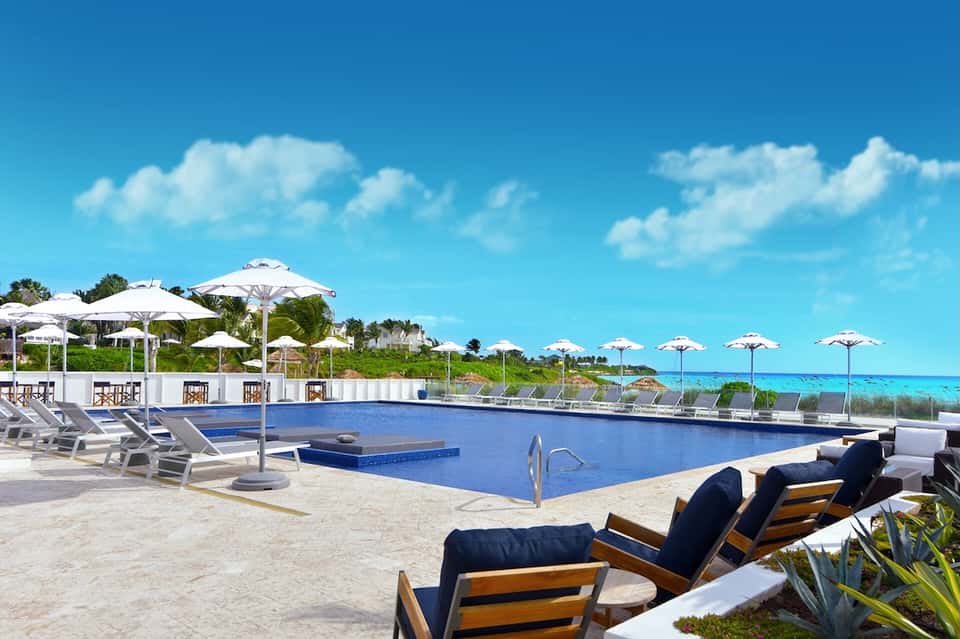 Oceanfront pool with white umbrellas, lounge chairs, and pristine turquoise water and beach