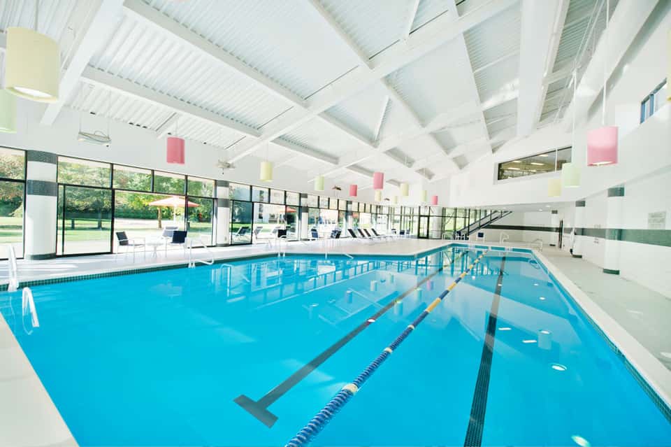 Indoor Olympic-size swimming pool with lane markers, white ceiling, and large windows overlooking grounds