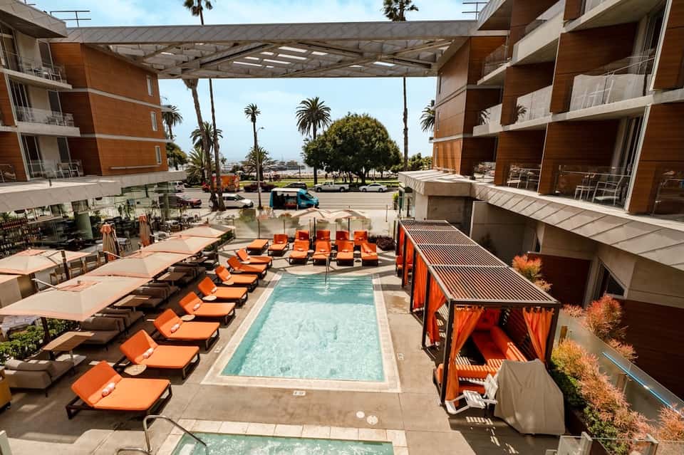 Resort courtyard pool with orange loungers, cabanas, and surrounding modern buildings