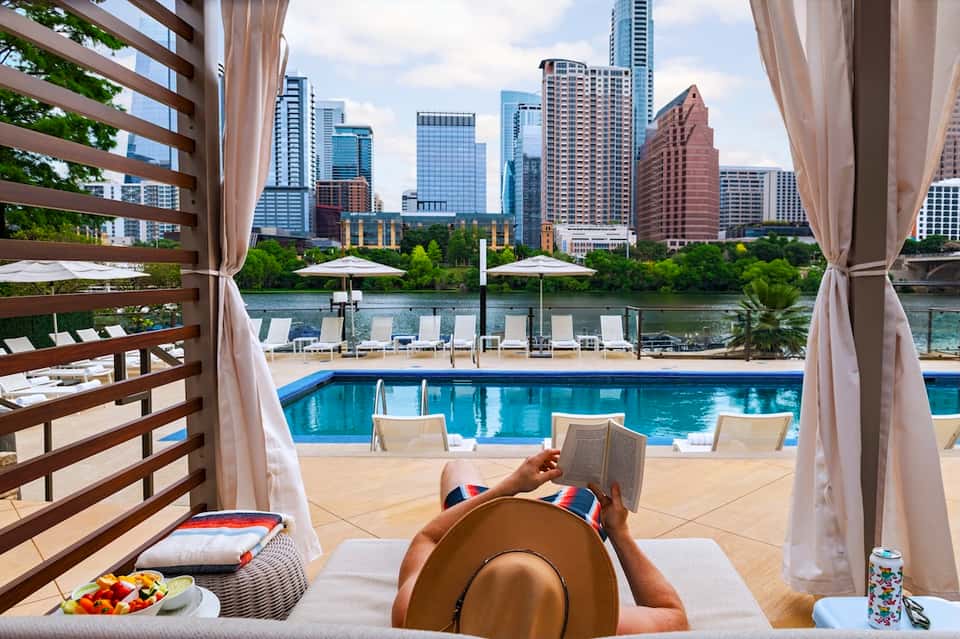 Urban resort pool lounge with city skyline views, private cabana, and waterfront backdrop