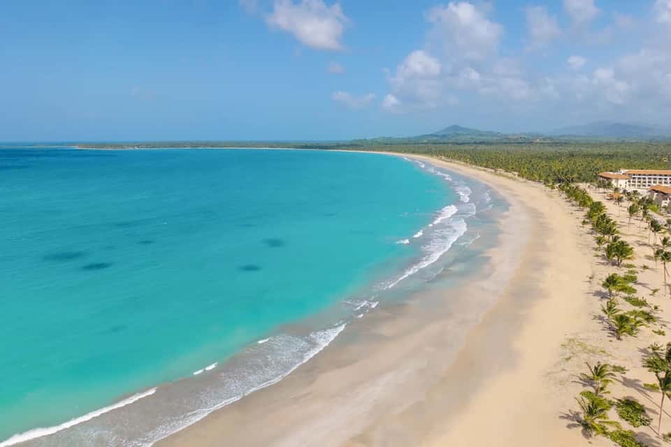 Aerial view of pristine turquoise beach with white sand, palm trees, and resort building