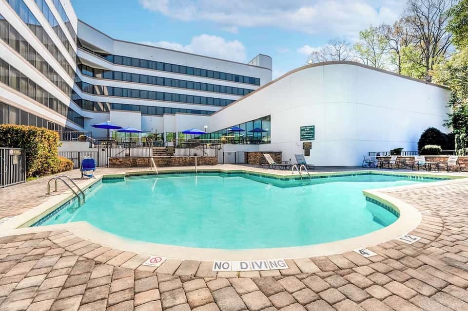 Resort swimming pool with blue umbrellas, modern curved building, and palm trees