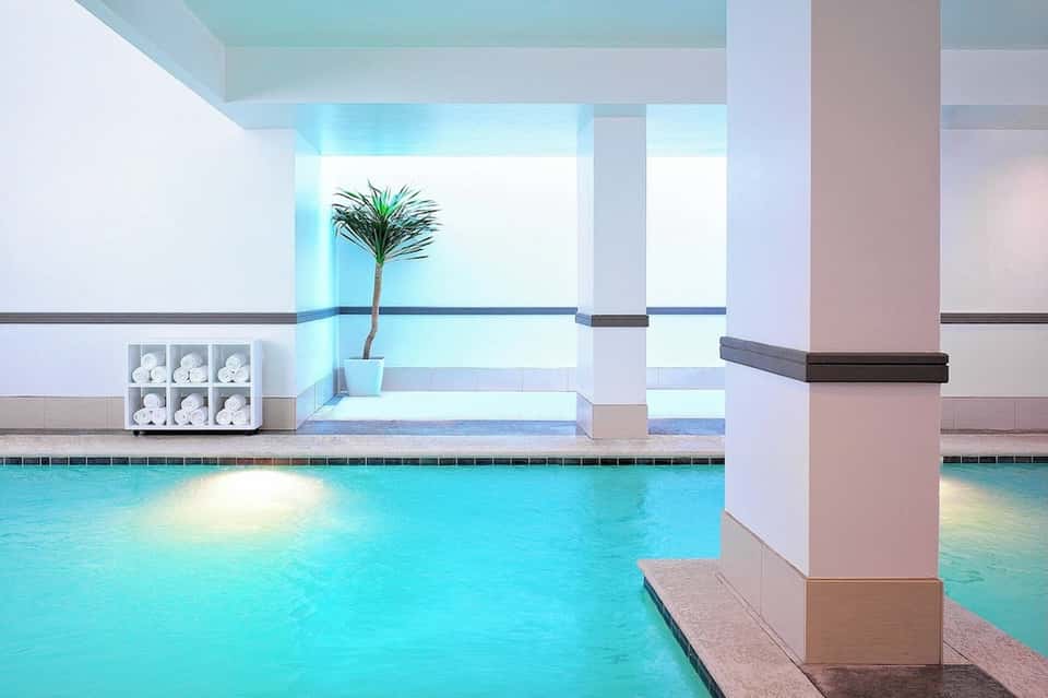 Indoor swimming pool with natural lighting, white columns, and spa-like minimalist design