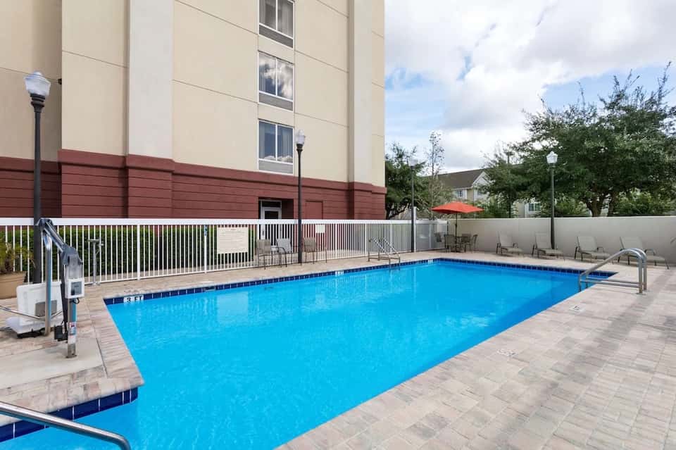 Rectangular hotel swimming pool with white safety fence, building exterior, and landscaping