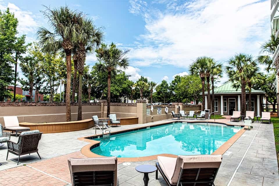 Resort pool surrounded by palm trees, lounge chairs, and modern building architecture