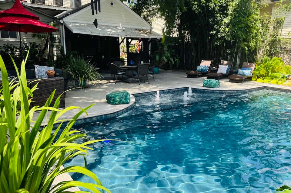 Resort backyard with curved swimming pool, tropical plants, red umbrella, and covered lounge seating area