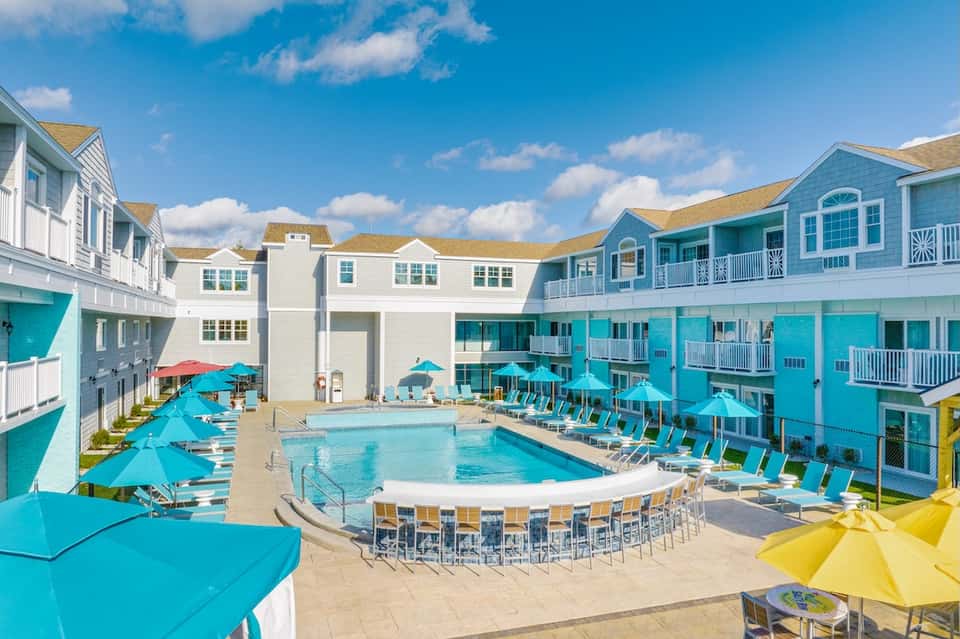 Colorful beachfront resort courtyard with turquoise pool, bright umbrellas, and coastal architecture