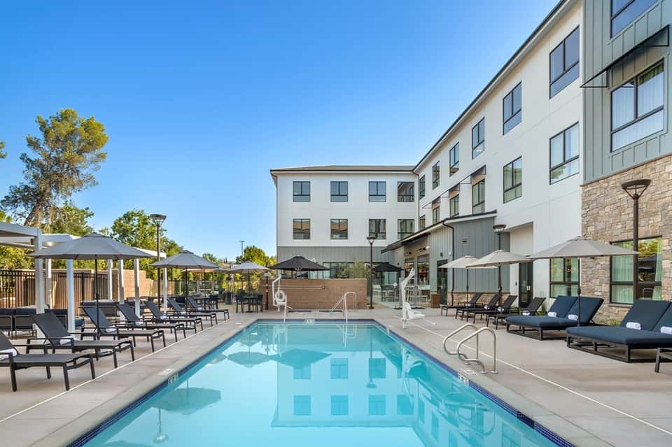 Hotel courtyard pool with lounge chairs, umbrellas, and modern building exterior