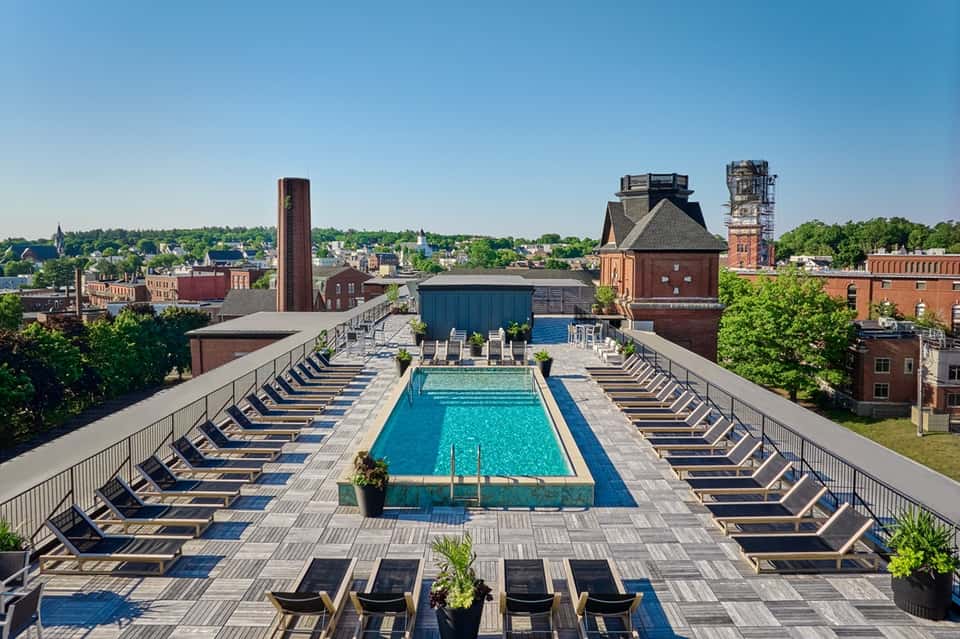 Rooftop lap pool with lounge chairs overlooking historic brick buildings and tree-lined cityscape