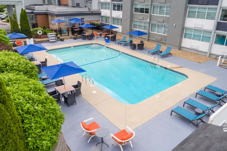 Residential pool area with blue umbrellas, loungers, and multi-story apartment buildings nearby