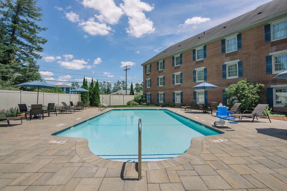 Outdoor swimming pool at brick hotel with lounge chairs, patio seating, and landscaping