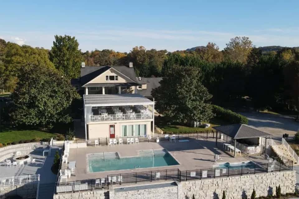 Aerial view of luxury home with pool, multi-level deck, and mature landscaping on wooded property