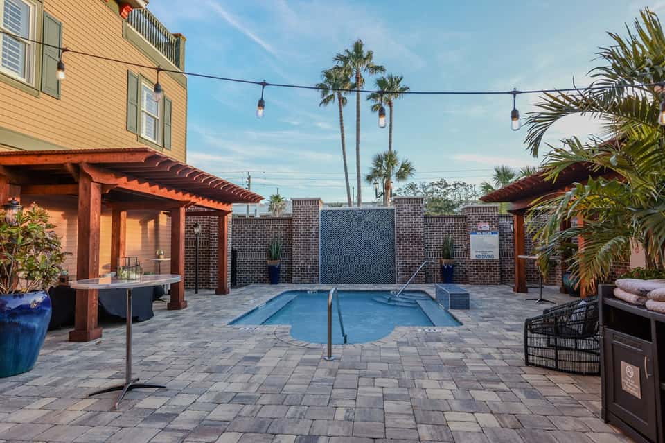 Courtyard with small heated pool, wooden pergola, and palm trees at dusk