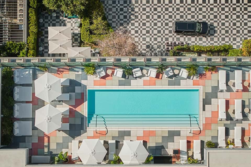 Aerial view of rooftop pool with turquoise water, white umbrellas, and colorful tile deck