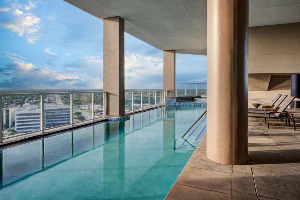 Indoor rooftop pool with turquoise water, panoramic city views, columns, and lounge chairs on deck