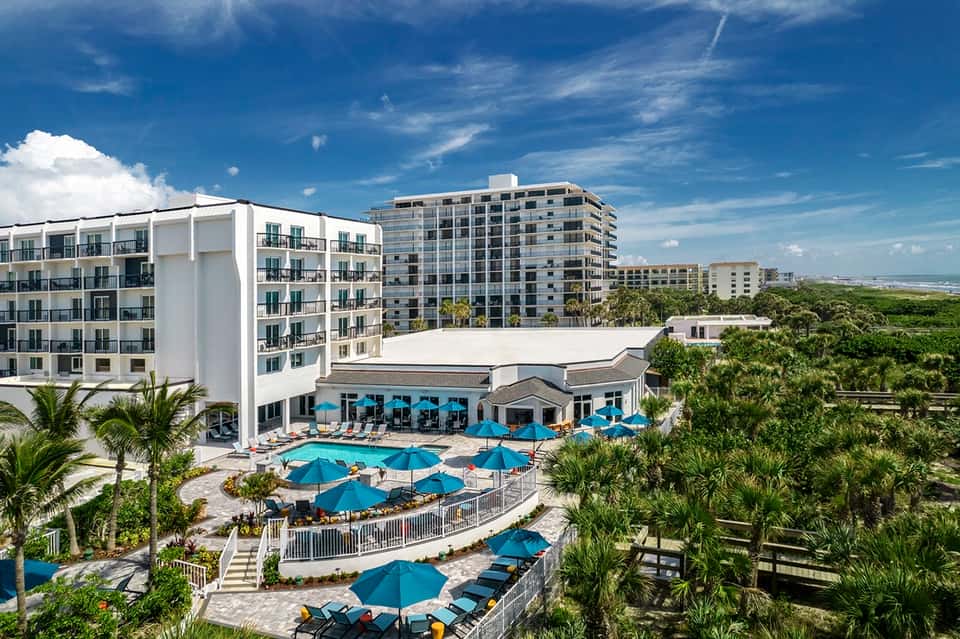 Resort buildings overlooking lagoon pool with blue umbrellas and palm landscaping