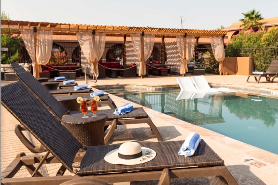 Luxury resort poolside with loungers, cabanas, and drinks on woven table