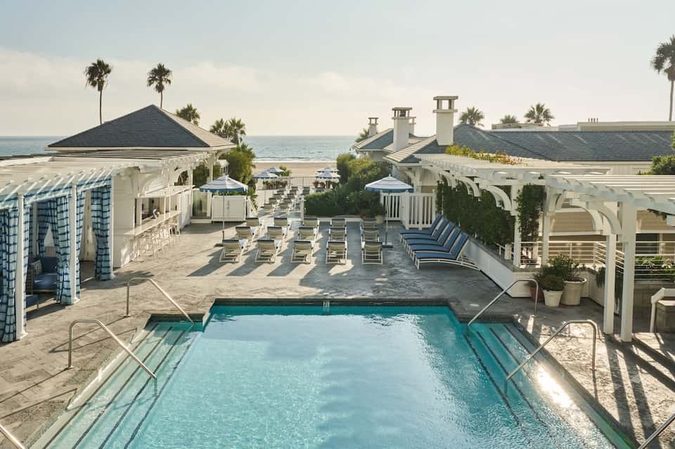 Oceanfront pool terrace with white pergolas, lounge seating, beach cabanas, and ocean view