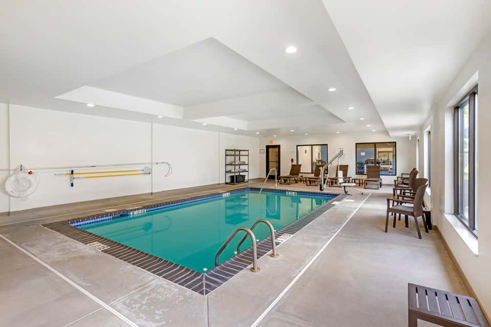 Indoor lap pool facility with bright ceiling, lounge seating, and glass doors leading to common areas