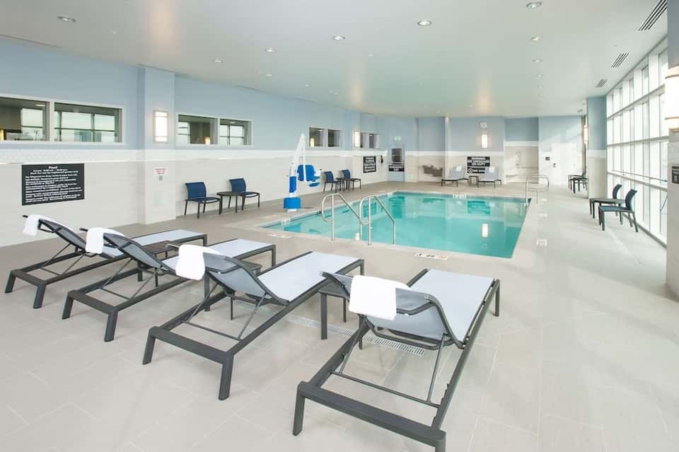 Indoor heated pool facility with lounge chairs, blue water, large windows, and modern amenities