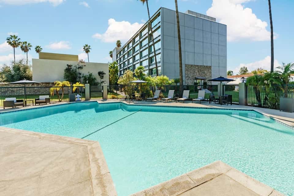 Resort swimming pool with turquoise water, lounge chairs, palm trees, and modern hotel building