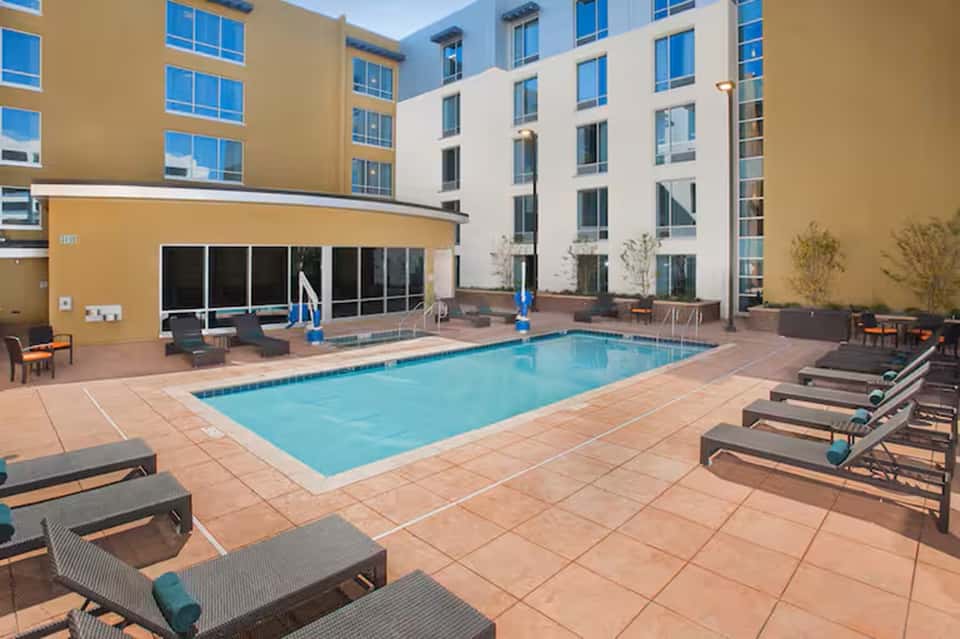 Resort courtyard pool with lounge chairs, metal decking, yellow building wing, and surrounding multi-story structures.