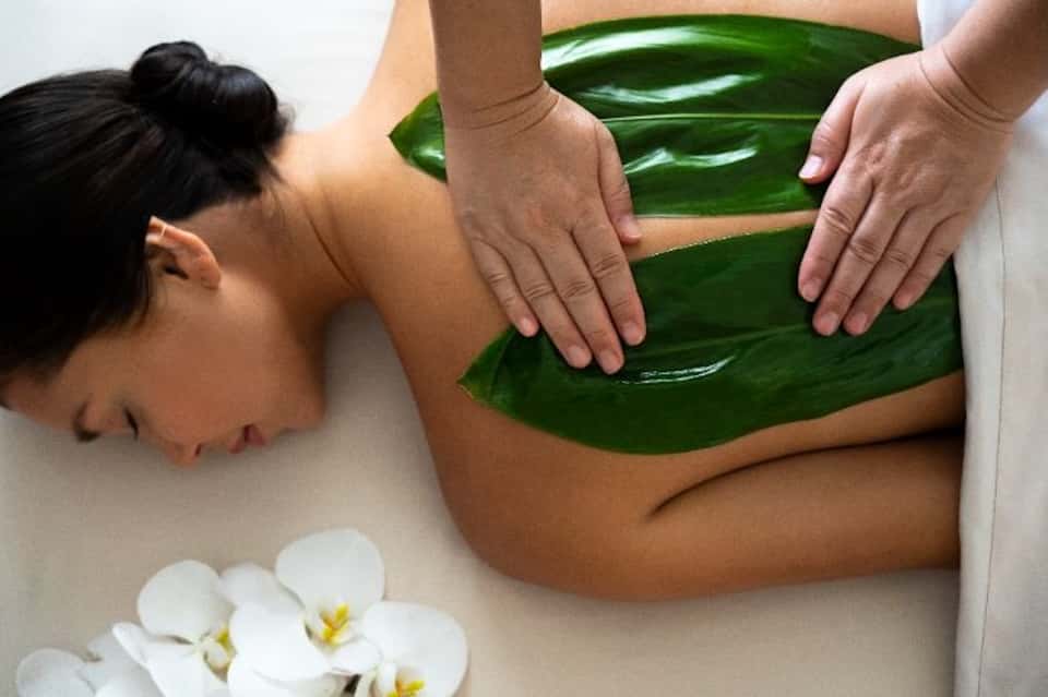Spa treatment showing hands performing green aloe vera wrap on client's back