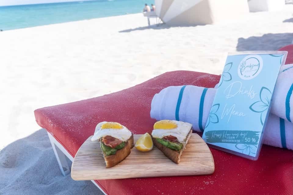 Beach scene with gourmet toast appetizers and blue menu card on red lounge chair by ocean